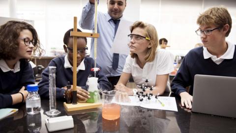 A group of students in a science lab watching as a teacher demonstrates an experiment.