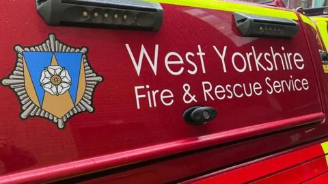 The side of a red vehicle with the words 'West Yorkshire Fire & Rescue Service' and a logo on the side.