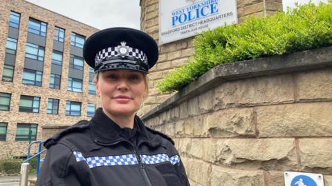 A female police officer in uniform wearing an inspector's peaked hat standing outside the entrance to a police station 