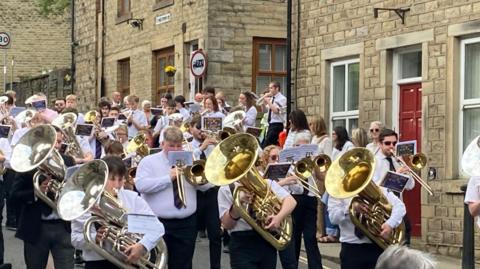 Lots of people in white shirts playing brass instruments as they walk through the street.