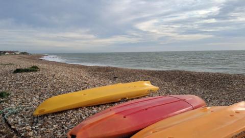 Three up-turned canoes lie on a beach with grey sea and cloudy blue sky