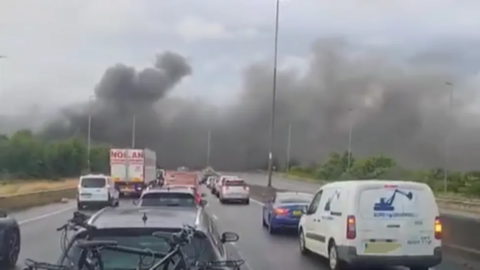 Cars parked on the motorway as black smoke pours out from behind trees 