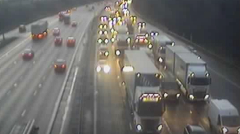 Travel builds up on the M6 with cars and lorries, with their lights on, come to a halt in the dark with traffic flowing on the other carriageway