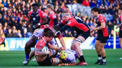 Action from Worcester Warriors v Cornish Pirates as a Pirates player is tackled to the ground still holding the ball and a Pirates lock prepares to jackle the second worcester defender.