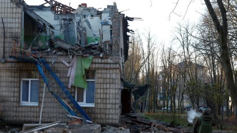 A police officer walks past a kindergarten that was heavily damaged by a drone strike. with a hollowed-out side.