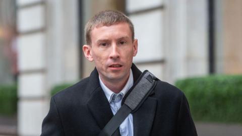 Chris Head, pictured outside wearing a black coat with a black bag strap across his body