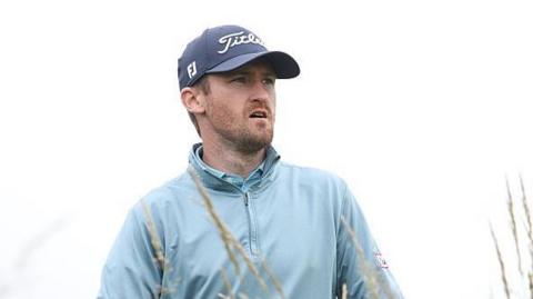 Andrew Wilson playing in The Open Final Qualifier at Dundonald Links, watching his ball as he wears a sky-blue wind-jammer 