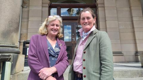 Two women stood outside a grey stoned building 