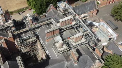 An drone-taken aerial view of scaffolding on top of a large red brick building