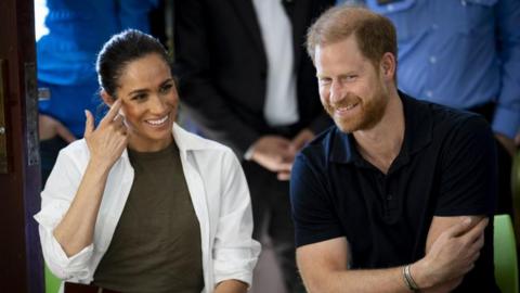 Prince Harry and Meghan sitting next to each other smiling