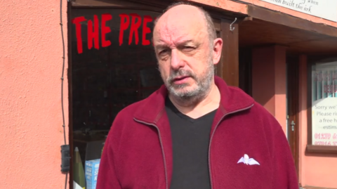 Owner of Prep Army surplus store in Cardigan, dressed in a red fleece