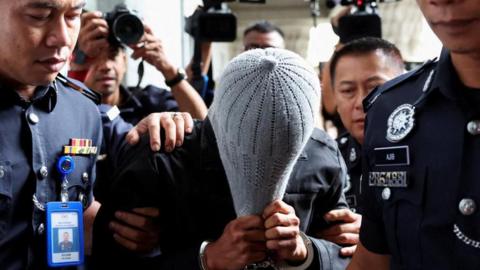 A man linked to Global Ikhwan Service and Business Holdings (GISB) covers his face as he is escorted by police officers after being charged in a court in Putrajaya, Malaysia September 18, 2024. 