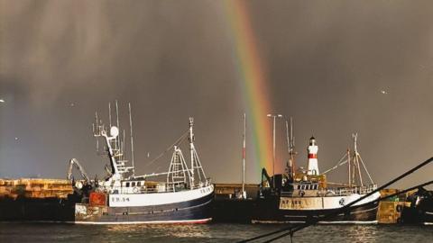 A rainbow above a harbour with two fishing boats in the foreground