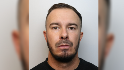 A mugshot of Khyl Harrington looking into the camera with short dark hair, dark eyes and a black top 