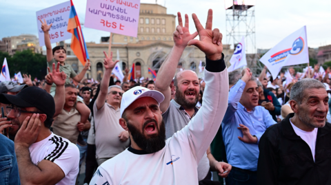 A crowd of people, appearing to be mainly men, wave flags and placards, with many raising their arms. They are identified as supporters of Strong Armenia, the party of billionaire Russian-Armenian businessman Samvel Karapetyan.