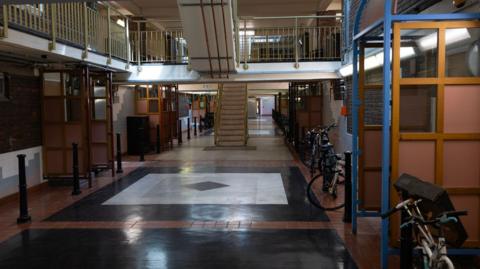 Interior view of a residential estate walkway with tiled floors, staircases, railings and several parked bicycles.