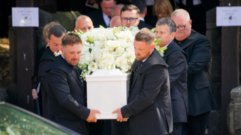 Men in black suits carrying a white coffin laden with white flowers