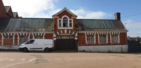A single storey brick building with a slanted roof. A white van is parked in front of the building.