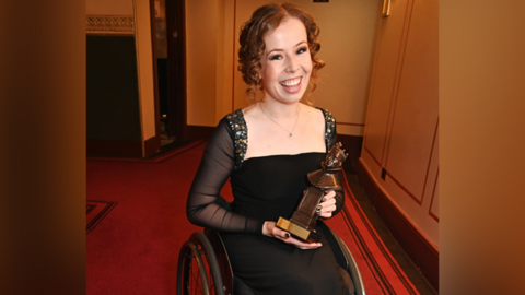 Amy Trigg wearing a black dress and smiling while holding her Olivier award