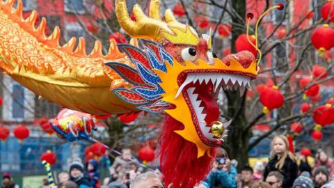 A traditional multi-coloured Chinese dragon in the middle of a parade surrounded by people