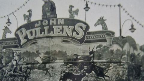 A black and white image of a fairground amusement banner with John Pullens written on it  