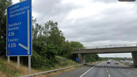 Three lane motorway with bridge over and blue junction sign on grass verge.