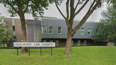 A Google Street image of a grey building with a sign in the foreground which says "Guildford Law Courts".