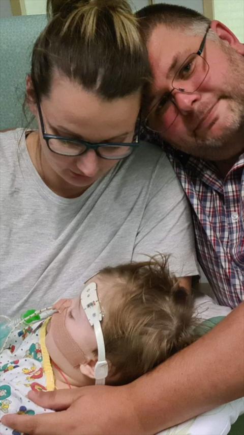 A man and a woman holding a toddler with a tube up their nose.