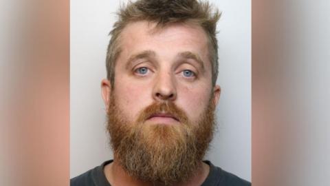 A mugshot of Stuart Miller. He has a ginger beard and blonde hair and has a blank expression.