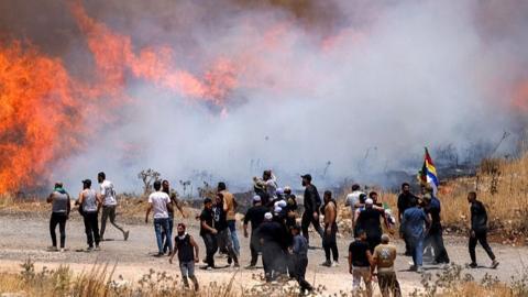Members of Syria's Druze community walk through tear gas fumes released by Israeli forces to disperse them, as they gather along the dividing line to attempt to cross the barbed-wire fence with the Israeli-annexed Golan Heights near Majdal Shams on July 16, 2025