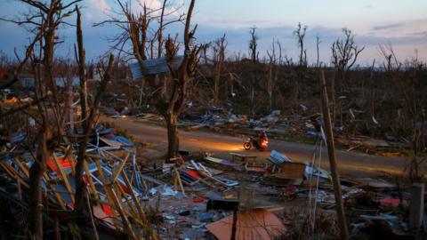 People ride a bike among debris in an area with no light in the aftermath of Hurricane Melissa in Auchindown, Saint Elizabeth Parish, Jamaica, November 4