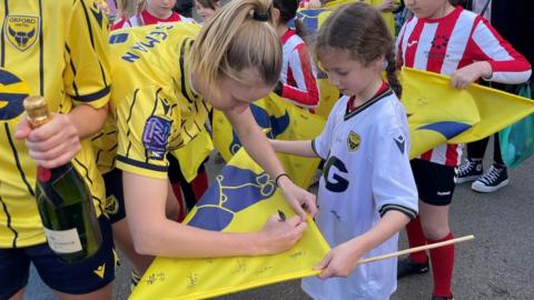 Oxford United player signing a flag for a girl
