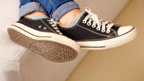 Close-up of the feet of someone wearing trainers on a pale-coloured sofa