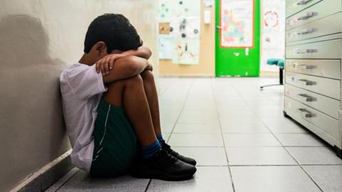 Stock image of a sad young boy sitting on the ground at school.