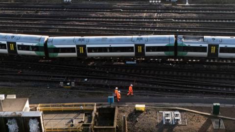 An aerial image showing a train that has come off the tracks and some engineers nearby wearing orange high-viz clothing