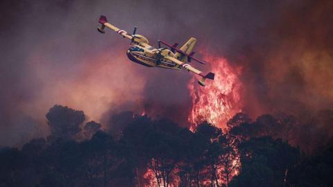 a small yellow airplane flies over flames. 