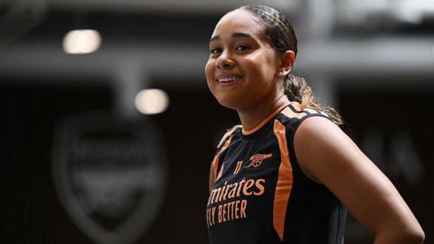 Olivia Smith smiles as she wears black and orange Arsenal training kit