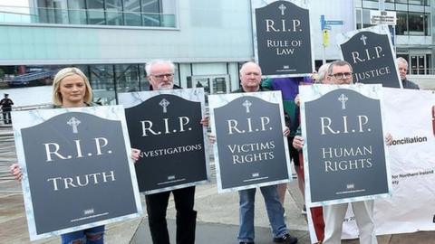 People hold signs reading R.I.P. truth, R.I.P investigations, R.I.P victims' rights and R.I.P human rights