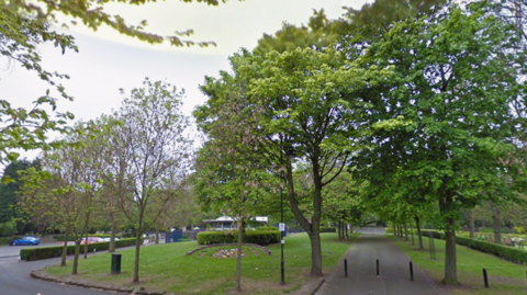 General view of Willenhall Memorial Park. There are several green-leafed trees around grey paths.