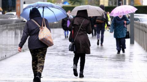 Pedestrians walk during a rainfall, holding umbrellas.