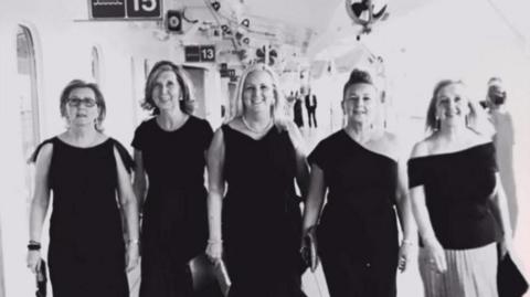 Five sisters Julie Madden, Christine Rushton, Carol Kenny, Maria Hewitt and Irene Ashworth all wearing black evening dresses and holding clutch handbags aboard Cunard's Queen Victoria cruise ship in 2018.