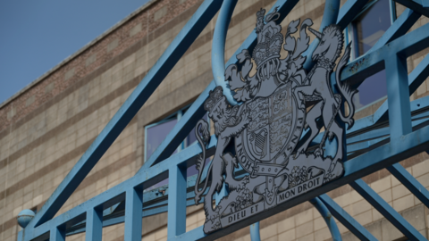 The entrance to Wolverhampton Crown Court. A blue metal frame is above the main door, with blue railings to the left of the shot.
