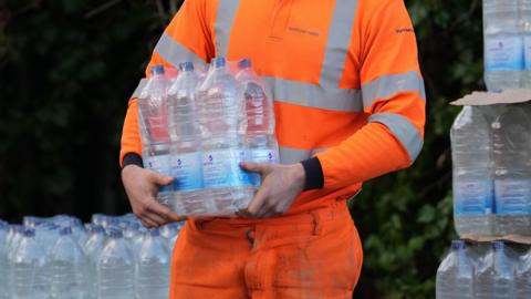 A South East Water worker in an orange hi-vi suit hands out bottled water
