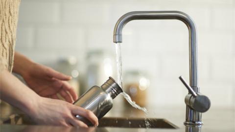 Person filling water bottled from kitchen tap