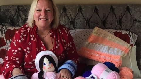 Susan Crossland surrounded by knitted items