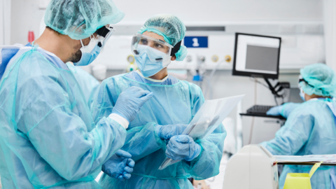 Two NHS healthcare workers stand in scrubs talking to each other