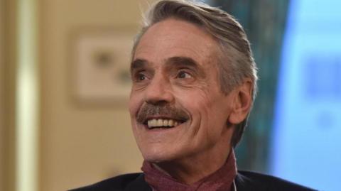 Actor Jeremy Irons smiling and looking off to the side of the picture.