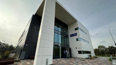 Cleveland Police headquarters in Hemlington - a white, multi-storey building with a small square in front and trees to the right. 