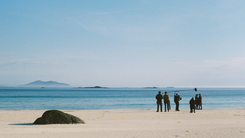 Filmeadh a' chiad sreath de An t-Eilean air tràigh sna Hearadh air là grianach. Chithear an criutha le camara agus mic air pòla mòr fada os cionn dithis de na cleasaichean 