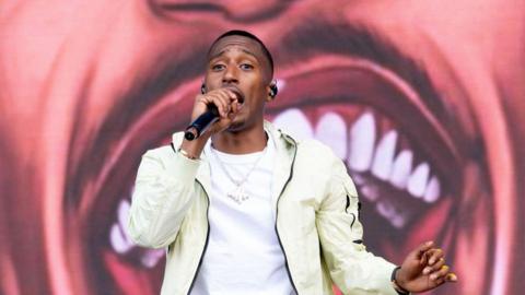 Yung Filly puts a microphone up to his mouth performing at Parklife Festival in Stone Island jacket and tshirt with chain